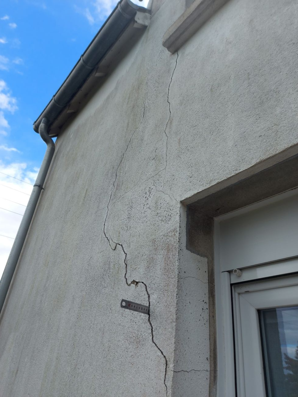 Fissure traversante sur une façade en parpaing due à une poussée de charpente sur le mur en pierre du pignon : 